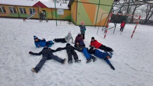 Grupa dzieci leżących na boisku pokrytym śniegiem.