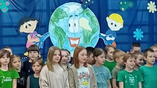 Uczniowie klas II a i II b śpiewają piosenkę ekologiczną. W tle niebieska dekoracja o Ziemi.