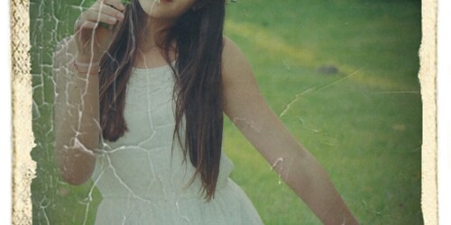 Dziewczynka w białej sukience klęczy na łące.