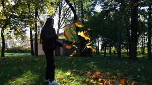 Uczennica w parku podrzuca liście, w tle budynek gospodarczy