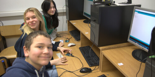 Usmeichnięci uczniowie siedzą przy komputerach i programują zadania do wykonania na mikrokontrolerze.