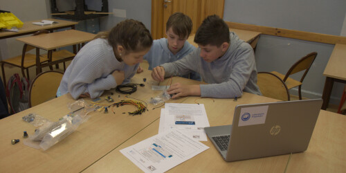 Uczniowie montują zestaw doświadczalny. Na stoli leży laptop, schematy oraz części do złożenia.