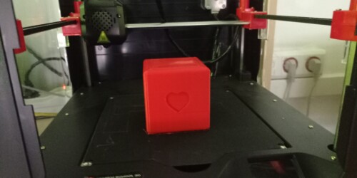 Czerwony sześcian stoi na stole drukarki 3D.
