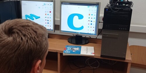 Uczeń modyfikuje parametry wydruku 3D litery C. W tle ekran komputera z wyświetlona literą C.