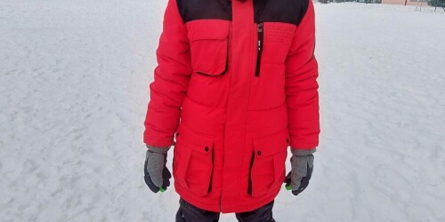 Dziecko w kurtce zimowej, czapce i rękawicach stoi na śniegu.