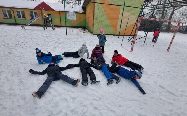 Grupa dzieci leżących na boisku pokrytym śniegiem.