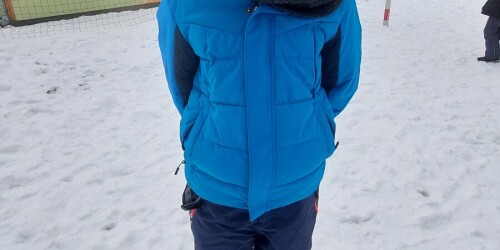 Dziecko w kurtce zimowej, czapce i rękawicach. Z tyłu kosz do koszykówki.