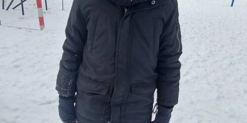 Dziecko w kurtce zimowej, czapce i rękawicach. Z tyłu kosz do koszykówki i bramka do piłki ręcznej.