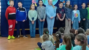 Uczniowie klasy III b śpiewają piosenkę na tle niebieskiej dekoracji.