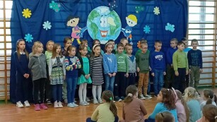 Uczniowie klasy I a śpiewają piosenkę. W tle niebieska dekoracja o Ziemi.