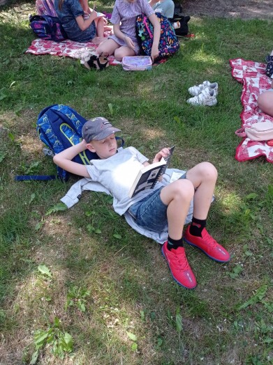 Uczeń leży na trawie oparty o plecak i czyta książkę.